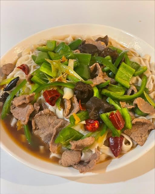 Hand-pulled noodles in beef broth with sliced beef, green peppers, wood ear mushrooms and dried chilies, served in a white bowl